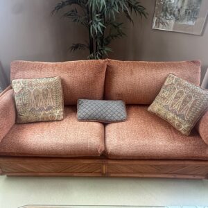 Vintage rattan frame sofa with rust upholstery and woven base detail.
