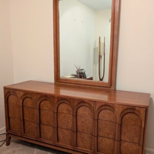 Wood dresser with arched panel drawer fronts and matching framed mirror.