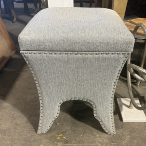 Gray herringbone upholstered vanity stool with nailhead trim and sculpted flared base.