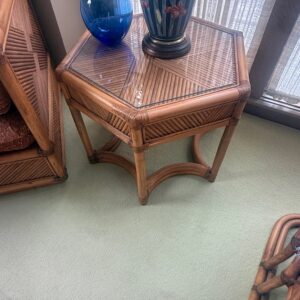 Hexagon rattan side table with glass top and curved base supports.