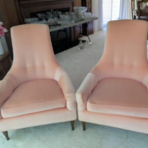 Set of two elegant accent chairs upholstered in a soft blush fabric, featuring a gently flared high back and subtle button tuft detailing. The sculpted silhouette and rolled arms create a refined, tailored look, while the plush seat cushions provide inviting comfort. Tapered wood legs add warmth and balance to the design. Perfect for a living room, bedroom, sitting area, or boutique-style space, these chairs bring sophistication with a touch of modern glamour.