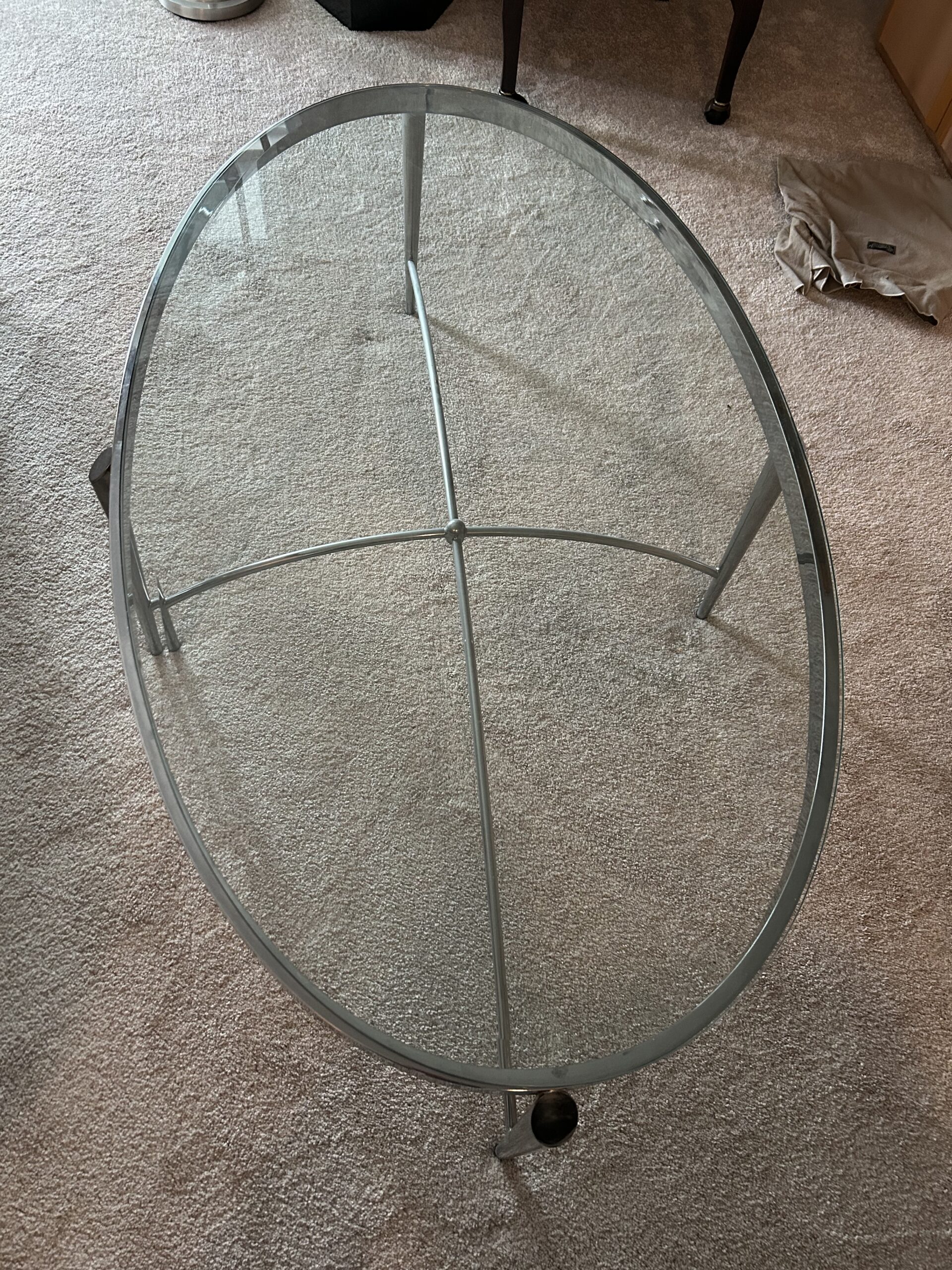 Oval glass coffee table with silver metal frame and crossbar base.